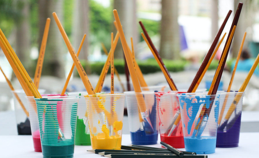 Cups with coloured paint and brushes and pencils